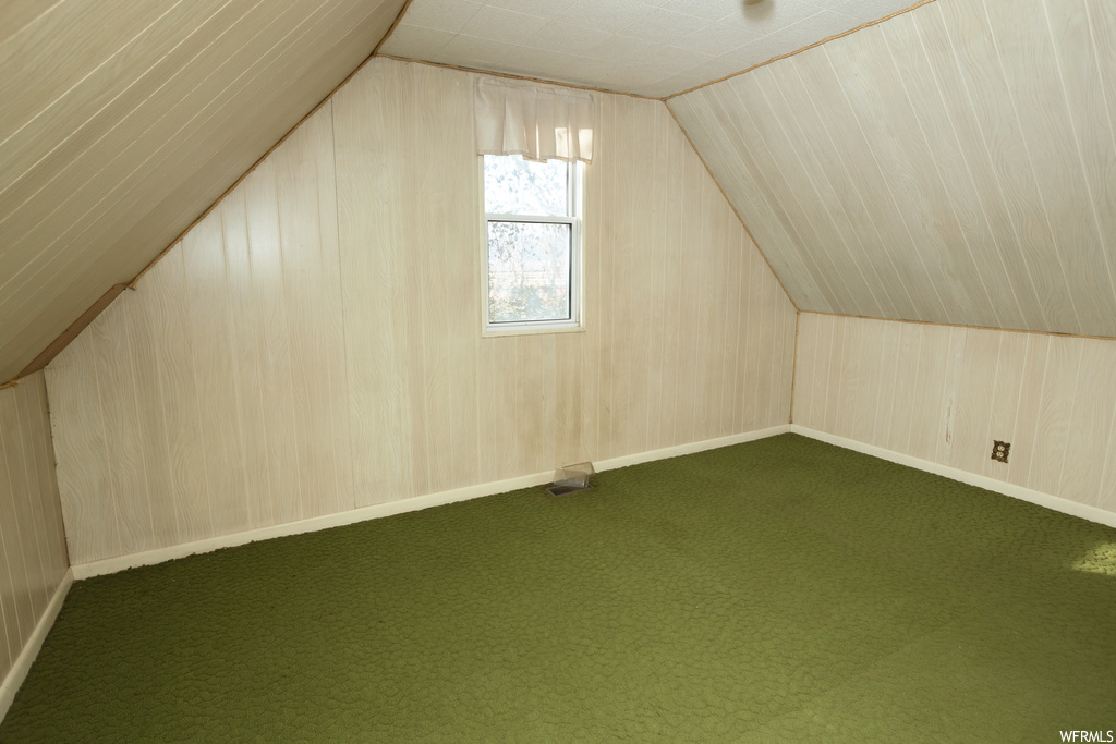 Additional living space with dark colored carpet, wooden walls, and vaulted ceiling
