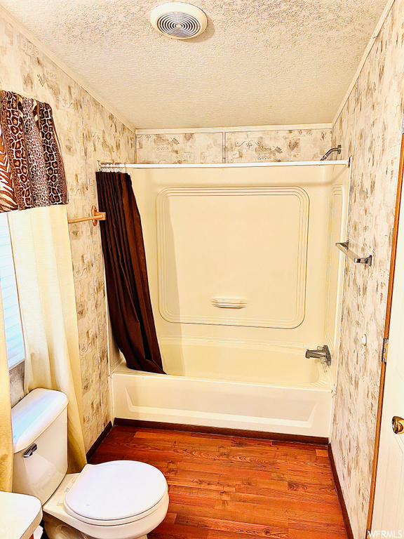 Bathroom featuring shower / bath combination with curtain, toilet, a textured ceiling, and hardwood / wood-style flooring