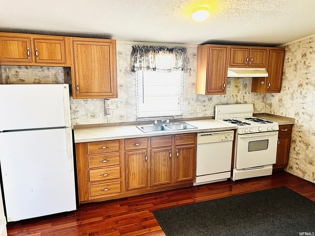Kitchen featuring sink, white appliances, dark wood-type flooring, and a textured ceiling