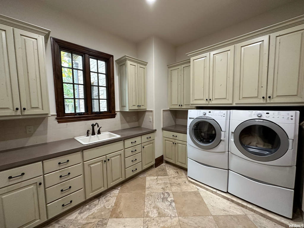 Clothes washing area featuring separate washer and dryer, cabinets, sink, and light tile floors