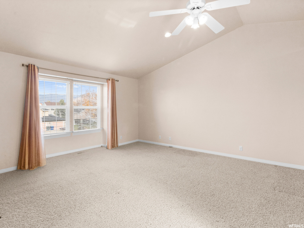 Carpeted spare room with ceiling fan and vaulted ceiling