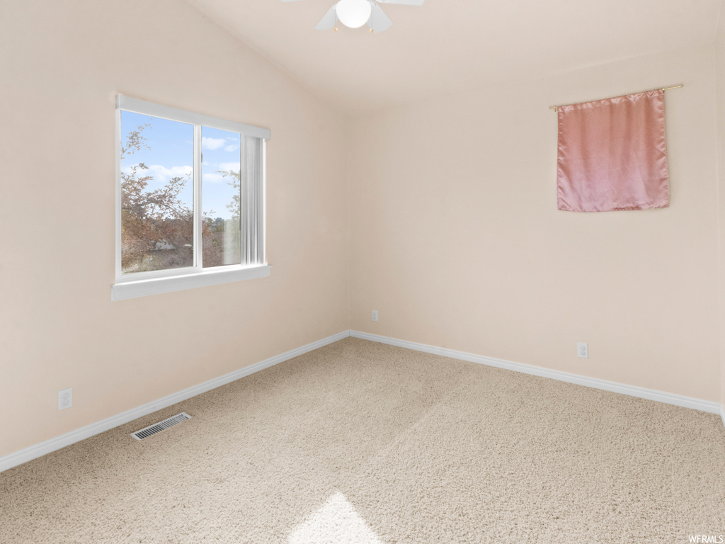 Carpeted spare room with ceiling fan and vaulted ceiling