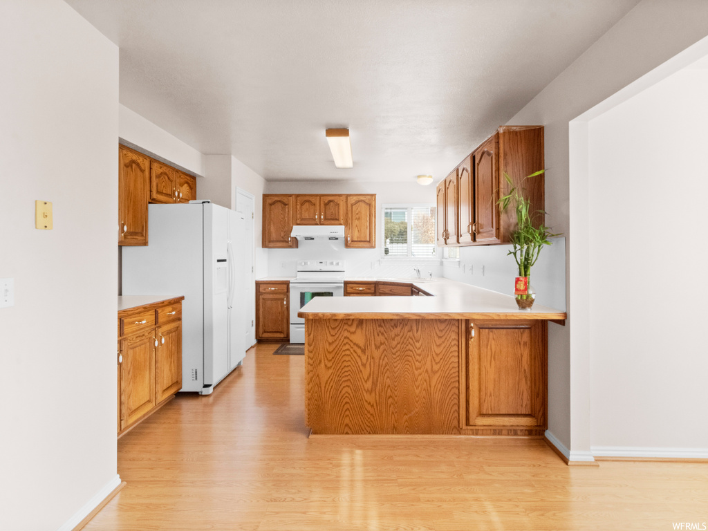 Kitchen with white appliances, kitchen peninsula, and light hardwood / wood-style floors