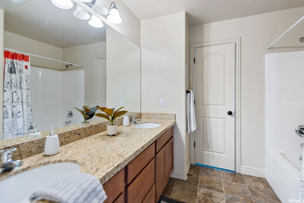 Bathroom featuring washtub / shower combination, vanity with extensive cabinet space, tile flooring, an inviting chandelier, and double sink