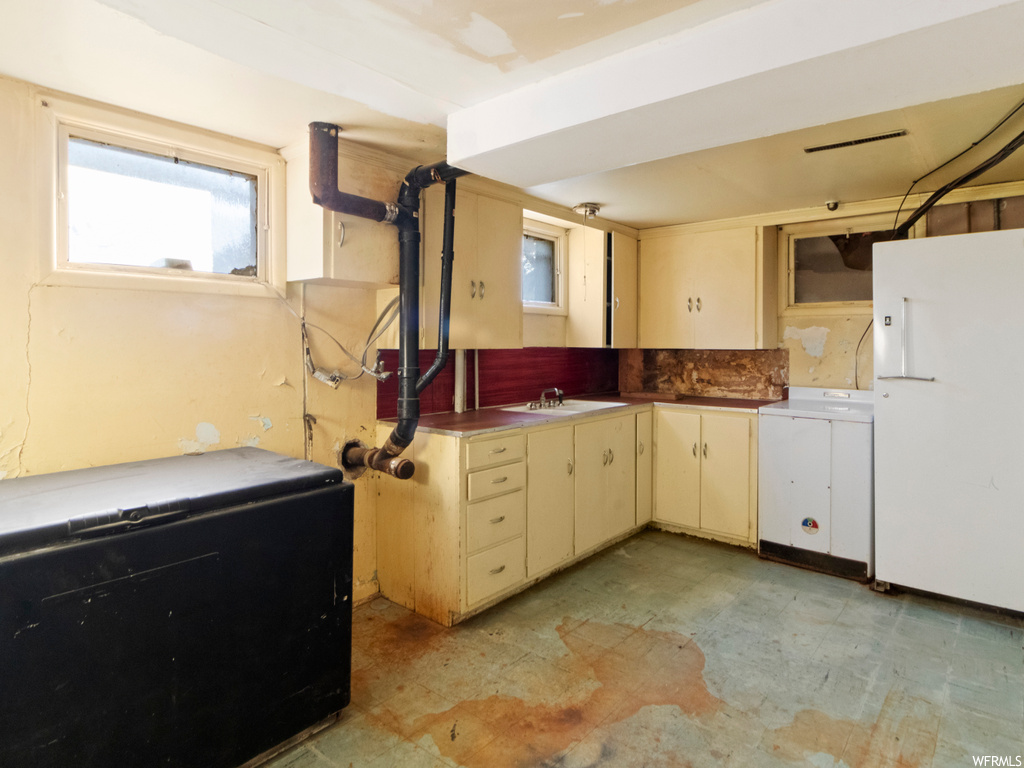 Kitchen with washer / dryer, sink, cream cabinets, and white fridge