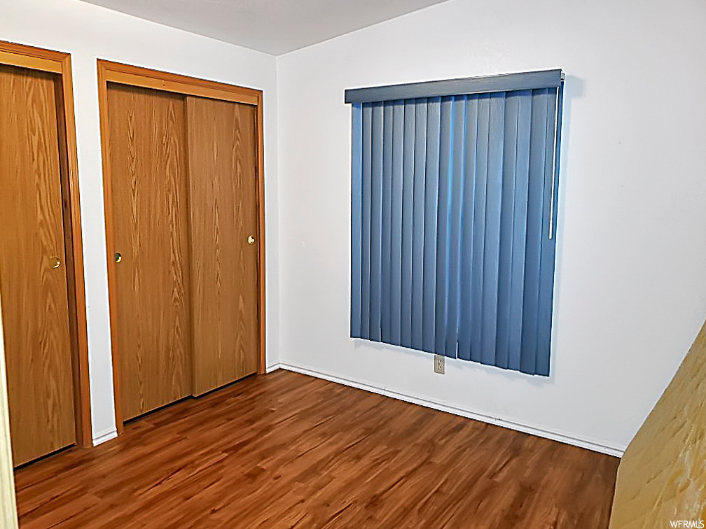 Unfurnished bedroom with dark wood-type flooring and two closets