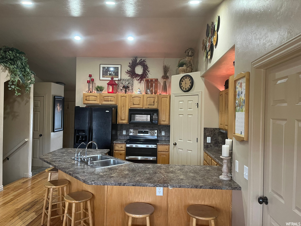 Kitchen with black appliances, tasteful backsplash, a breakfast bar area, and light hardwood / wood-style flooring