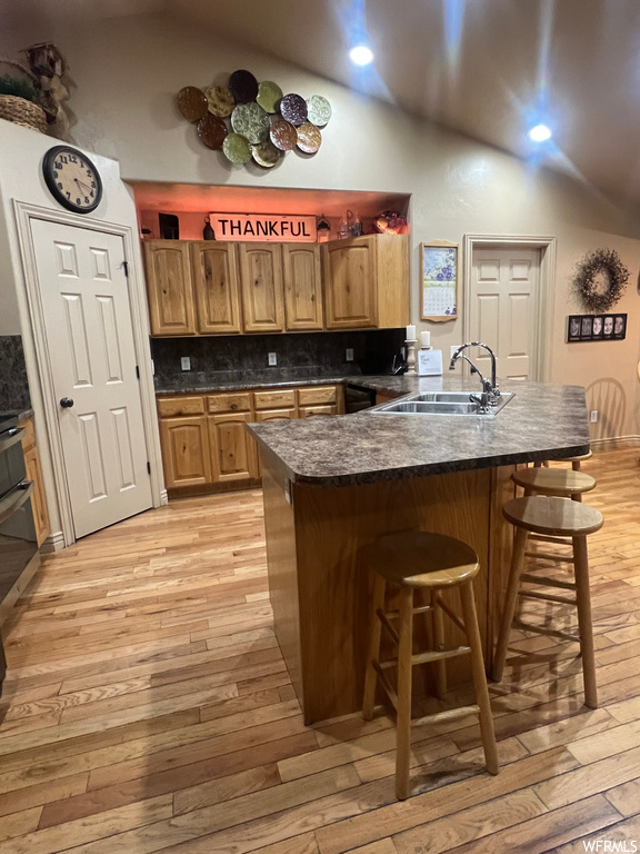Kitchen with sink, a breakfast bar area, backsplash, light hardwood / wood-style flooring, and a kitchen island
