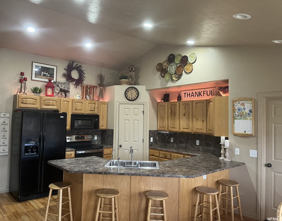 Kitchen featuring sink, a kitchen breakfast bar, kitchen peninsula, black appliances, and tasteful backsplash