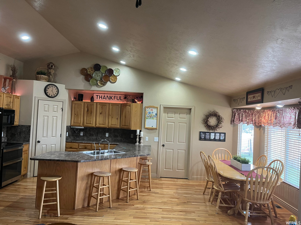 Kitchen with sink, light hardwood / wood-style flooring, a kitchen bar, kitchen peninsula, and tasteful backsplash