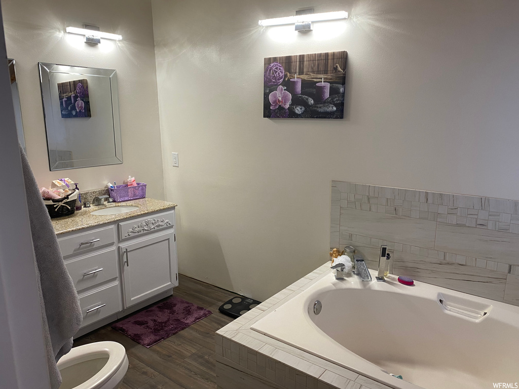 Bathroom featuring toilet, vanity, a relaxing tiled bath, and wood-type flooring