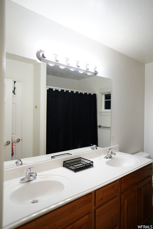 Bathroom with toilet, a textured ceiling, and double vanity