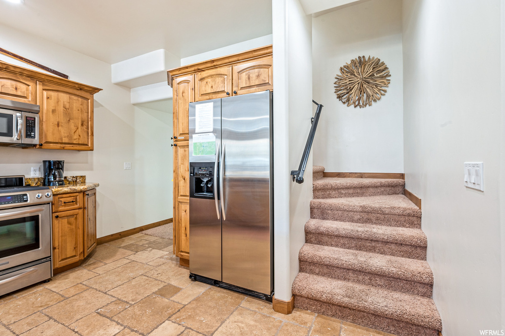 Kitchen with light tile floors, appliances with stainless steel finishes, and light stone countertops