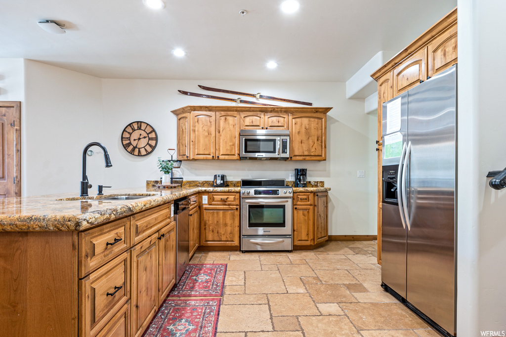 Kitchen with sink, light tile flooring, appliances with stainless steel finishes, light stone countertops, and kitchen peninsula