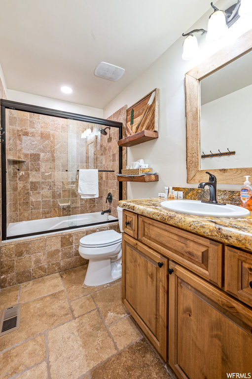 Full bathroom featuring toilet, tile flooring, combined bath / shower with glass door, and oversized vanity