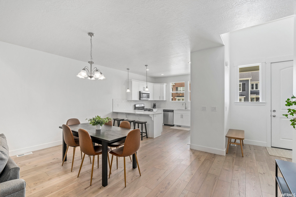 Dining room featuring light hardwood / wood-style floors, a textured ceiling, a notable chandelier, and sink