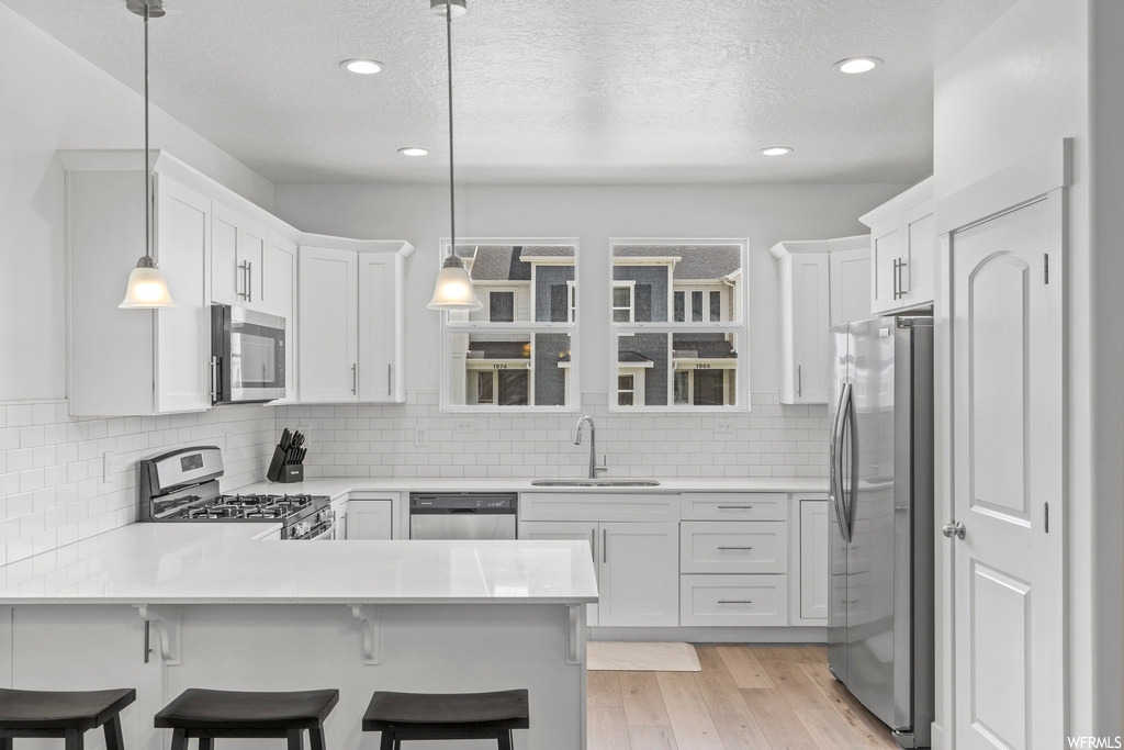 Kitchen featuring light hardwood / wood-style floors, sink, hanging light fixtures, and stainless steel appliances