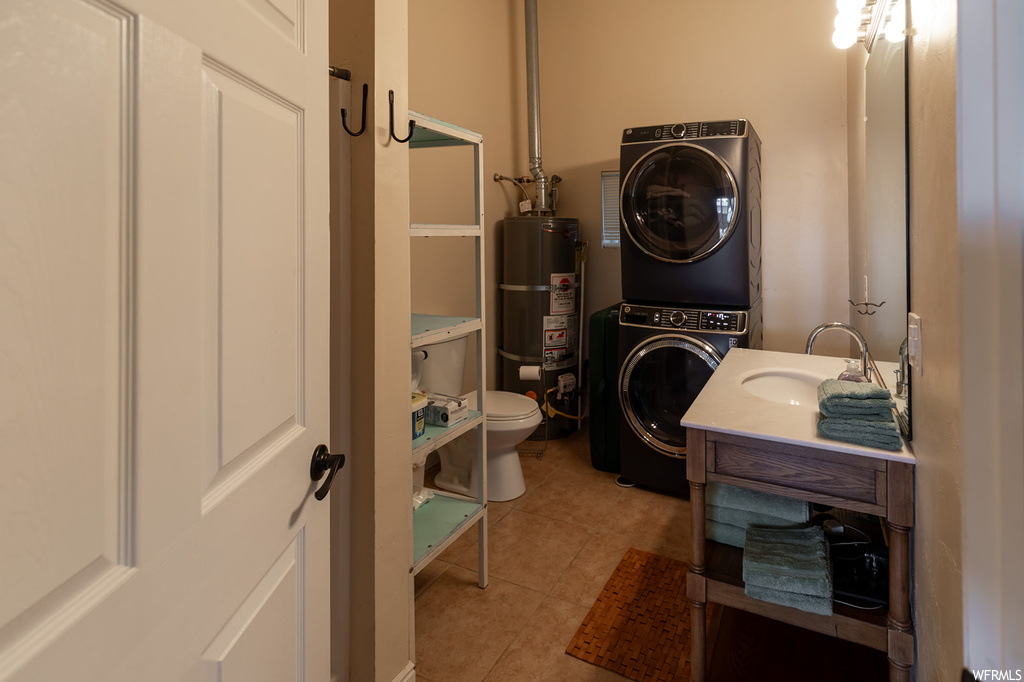 Bathroom featuring toilet, stacked washer and dryer, secured water heater, tile floors, and vanity