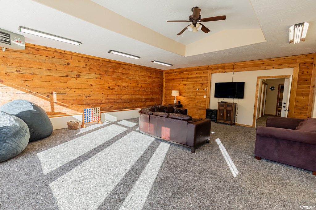 Carpeted living room featuring wood walls and ceiling fan