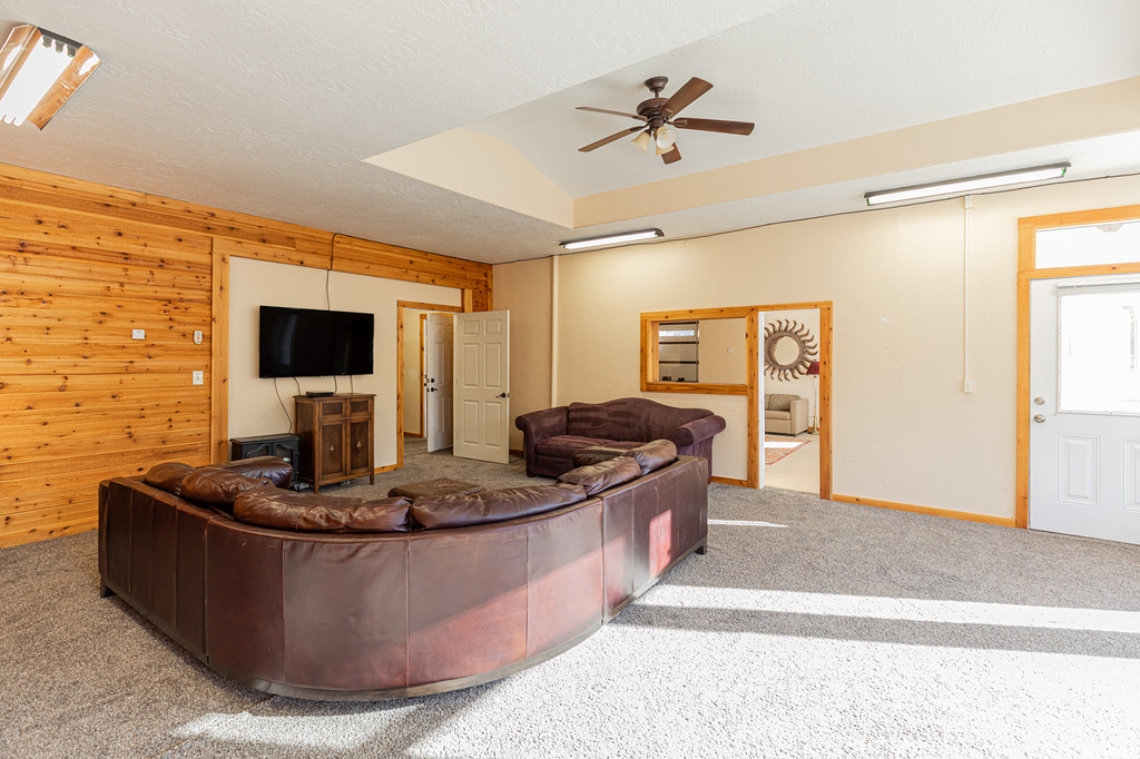 Carpeted living room with ceiling fan and wood walls
