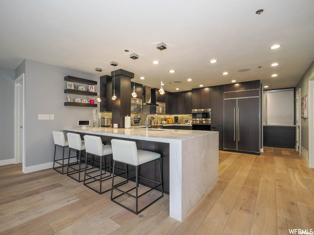 Kitchen featuring wall chimney exhaust hood, backsplash, light wood-type flooring, and paneled fridge