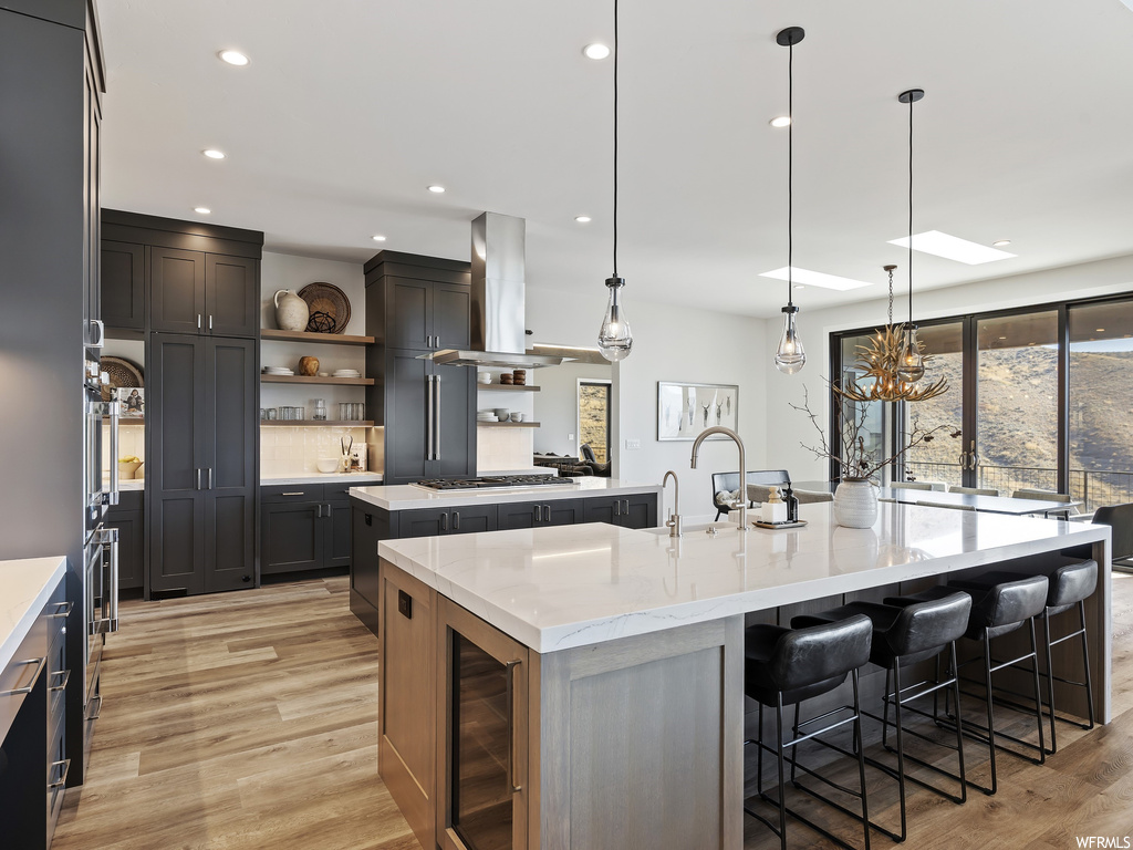 Kitchen featuring light wood-type flooring, hanging light fixtures, island exhaust hood, and an island with sink