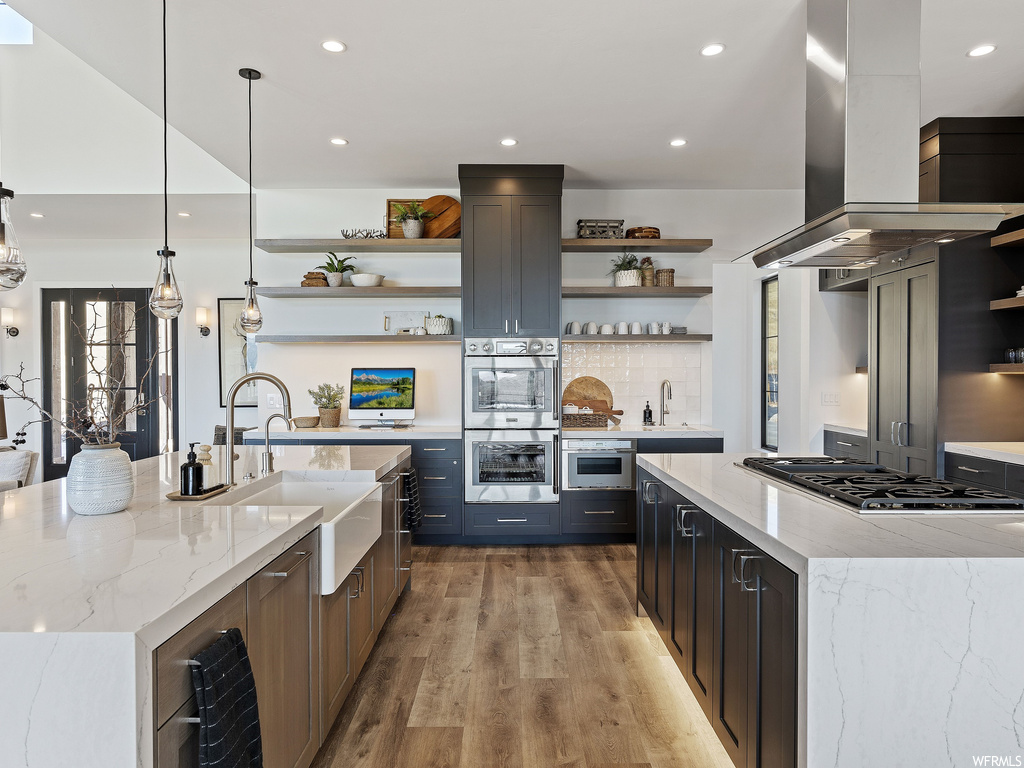 Kitchen with hanging light fixtures, a center island with sink, island range hood, and light hardwood / wood-style floors