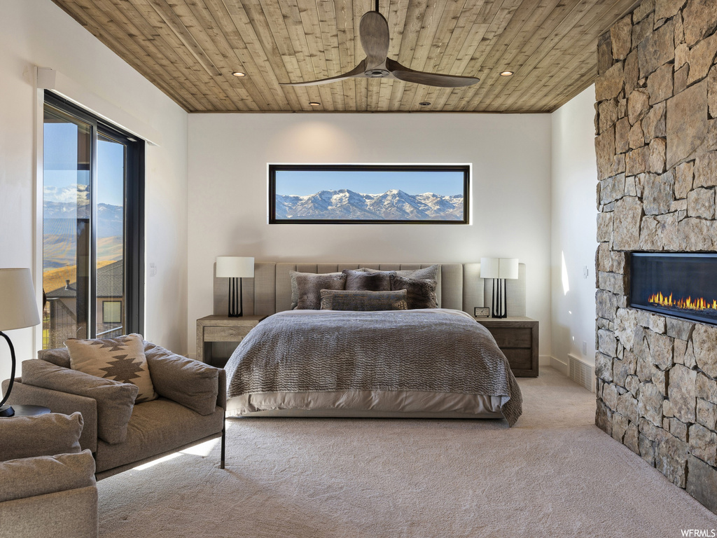 Carpeted bedroom featuring ceiling fan, wood ceiling, access to outside, and a stone fireplace