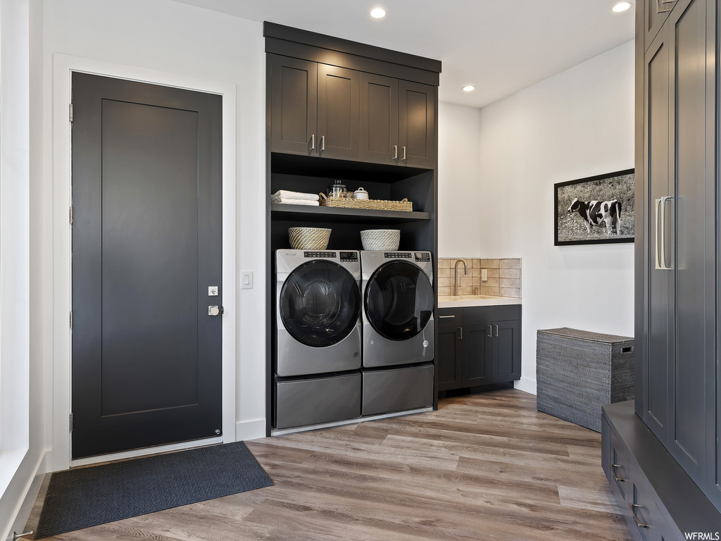 Washroom with cabinets, washing machine and clothes dryer, sink, and light hardwood / wood-style floors