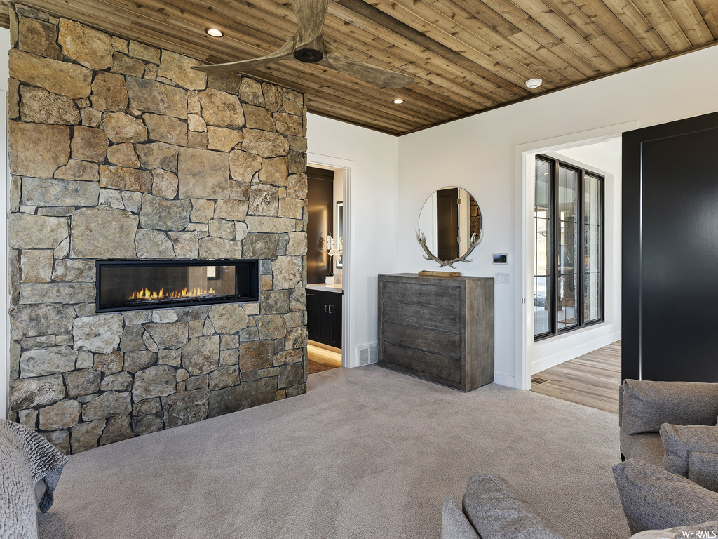 Living room with wood ceiling, light colored carpet, and a stone fireplace