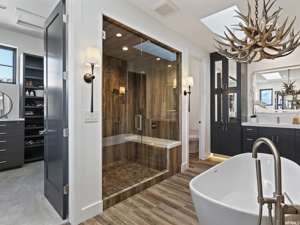 Bathroom with a healthy amount of sunlight, a notable chandelier, walk in shower, wood-type flooring, and oversized vanity