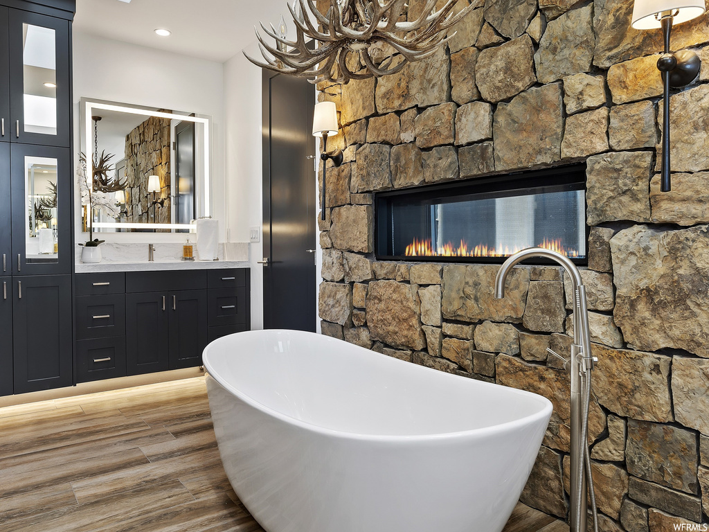 Bathroom featuring a bathing tub, hardwood / wood-style flooring, a stone fireplace, and vanity