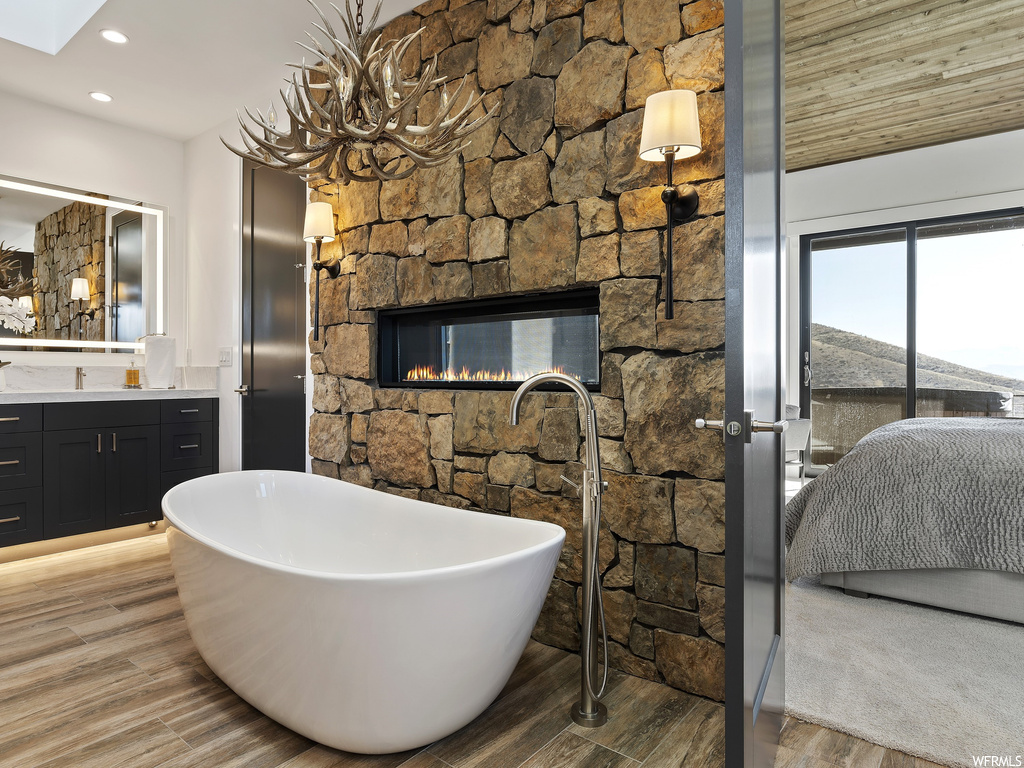 Bathroom featuring a tub, wood-type flooring, a stone fireplace, and vanity