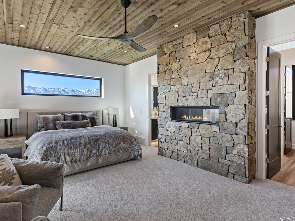 Bedroom with wooden ceiling, light carpet, ceiling fan, and a stone fireplace