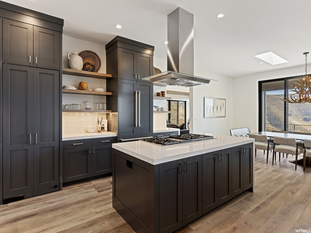 Kitchen featuring a healthy amount of sunlight, a notable chandelier, island exhaust hood, and pendant lighting