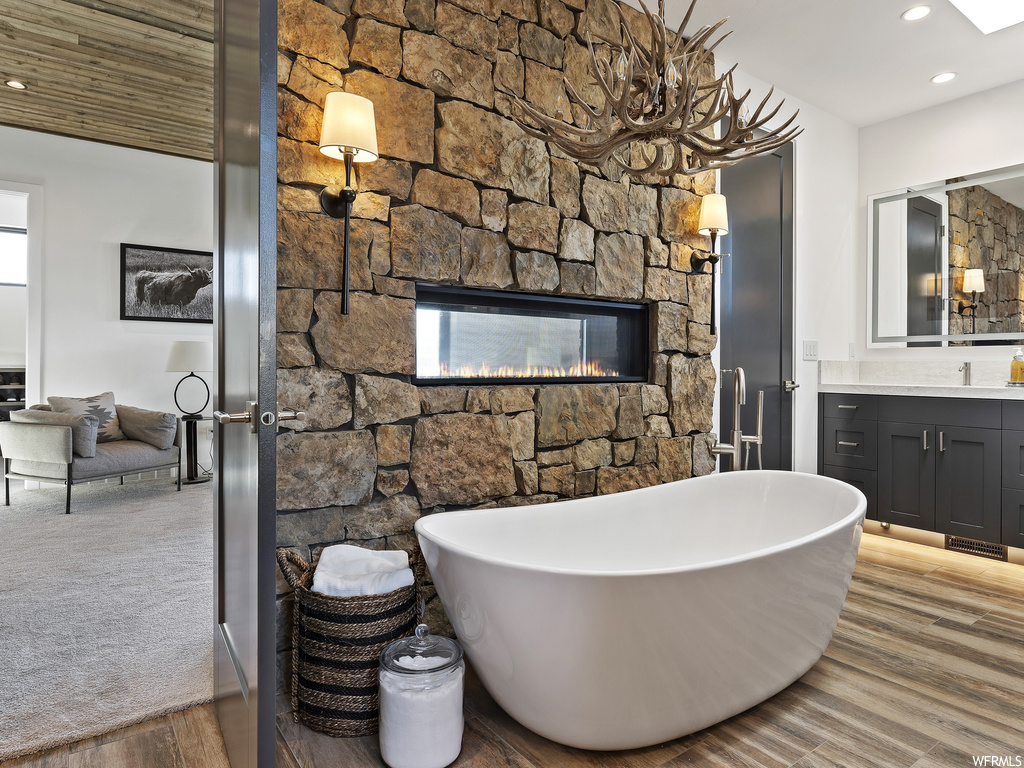 Bathroom featuring vanity, a fireplace, wood-type flooring, and a bathing tub