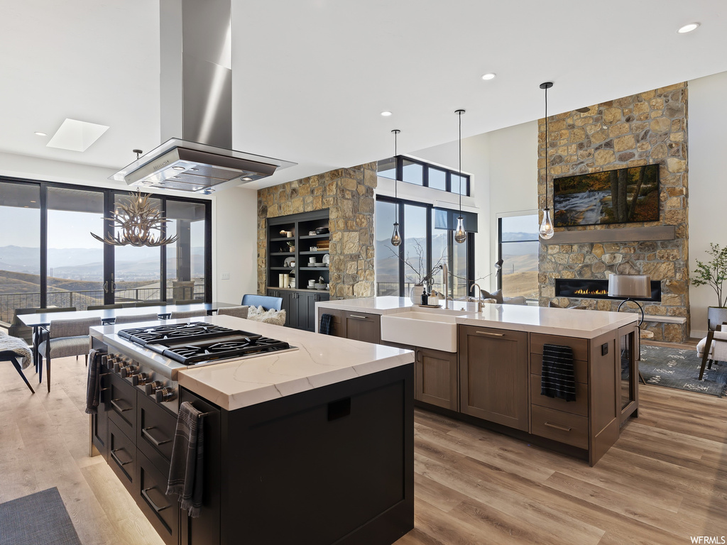 Kitchen with a notable chandelier, light hardwood / wood-style floors, decorative light fixtures, island range hood, and a center island with sink