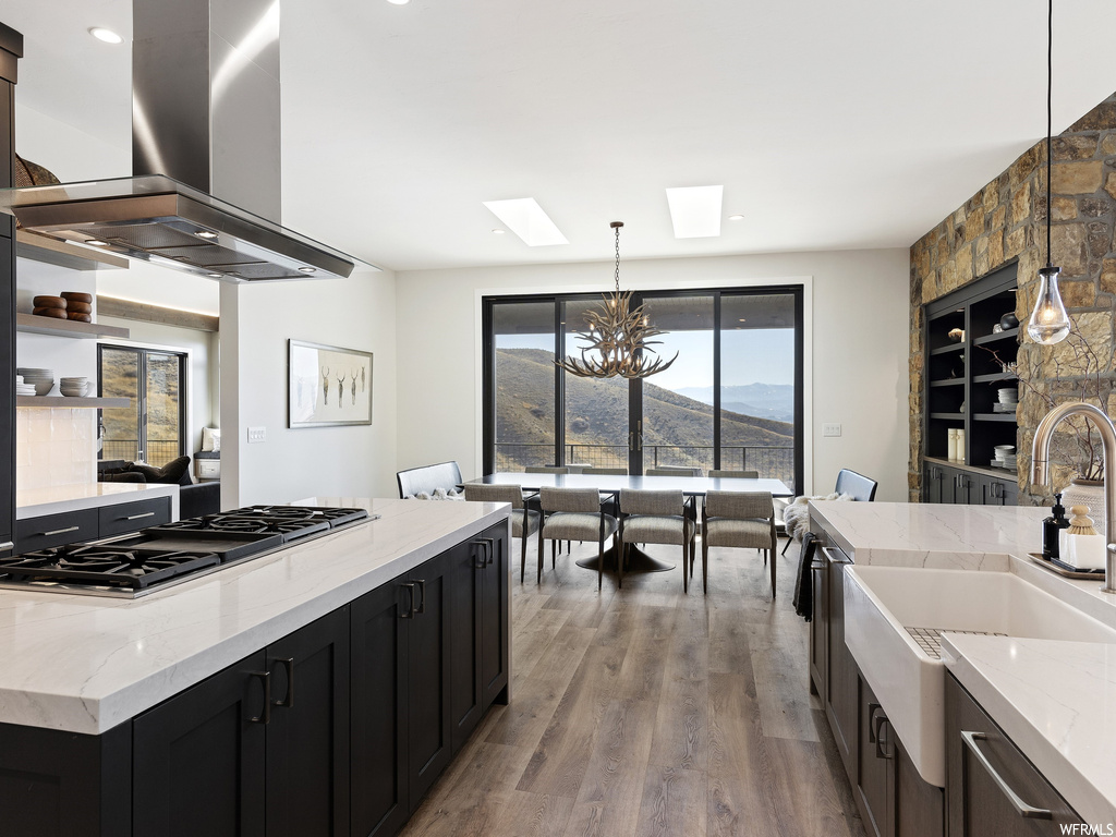 Kitchen with black gas stovetop, island exhaust hood, a chandelier, hanging light fixtures, and light wood-type flooring