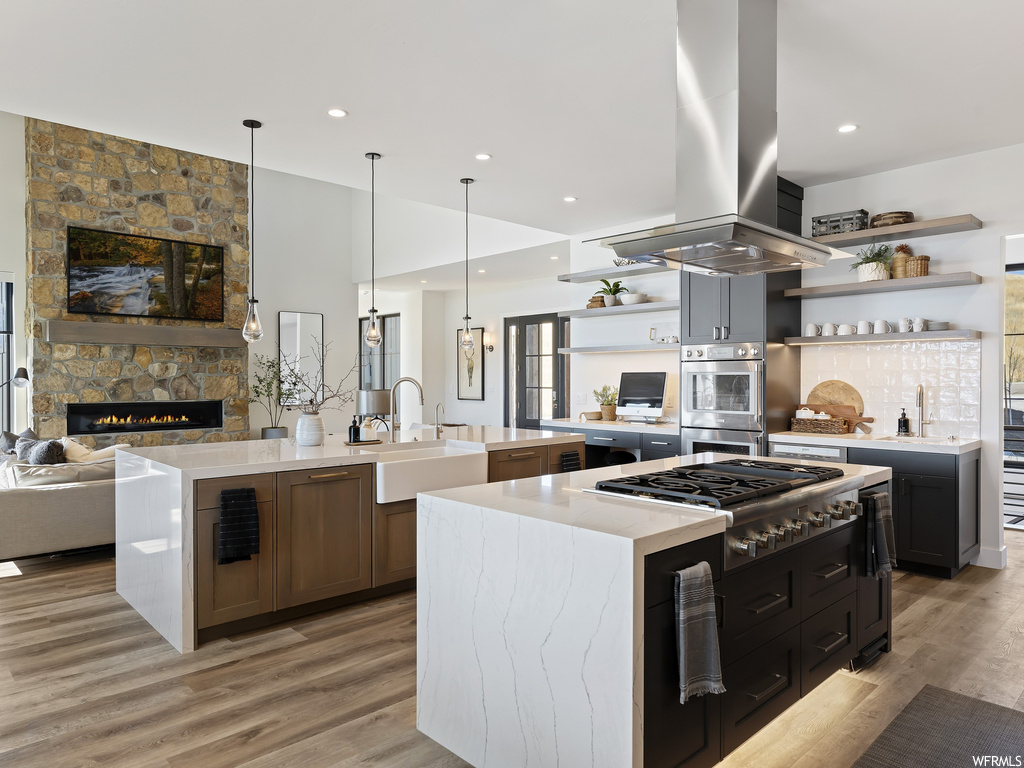 Kitchen with sink, island exhaust hood, light hardwood / wood-style flooring, a center island with sink, and pendant lighting