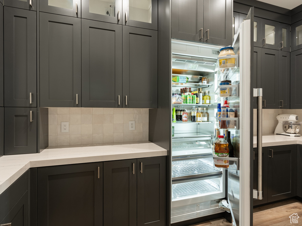 Kitchen with refrigerator, light wood-type flooring, light stone countertops, and backsplash