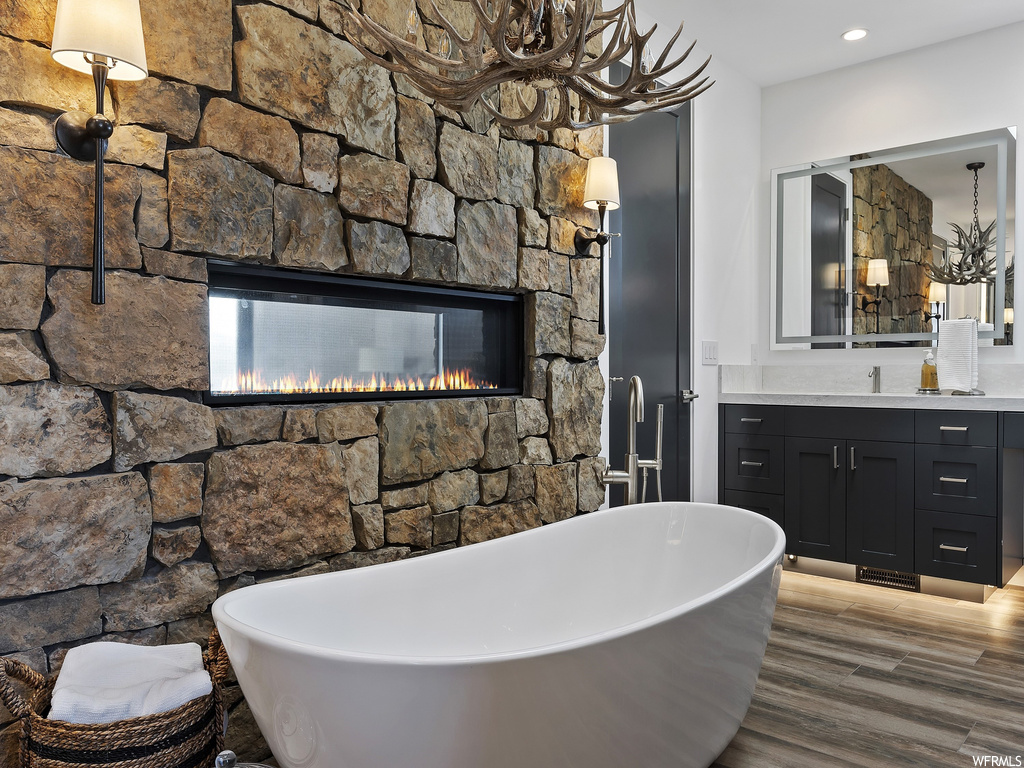 Bathroom featuring a bath, wood-type flooring, an inviting chandelier, a fireplace, and vanity