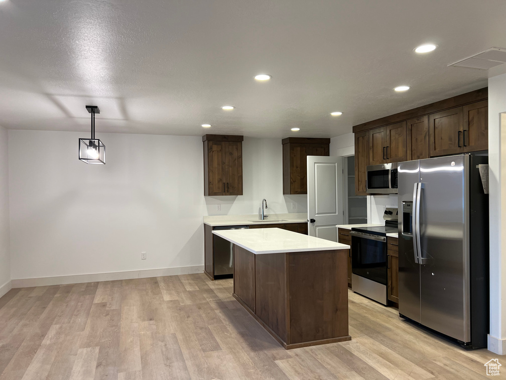 Kitchen featuring a kitchen island, pendant lighting, appliances with stainless steel finishes, and light hardwood / wood-style flooring