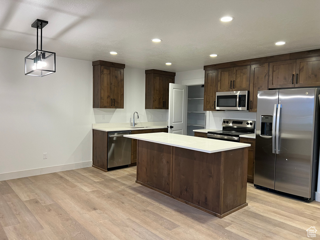 Kitchen featuring decorative light fixtures, stainless steel appliances, dark brown cabinetry, a center island, and light wood-type flooring