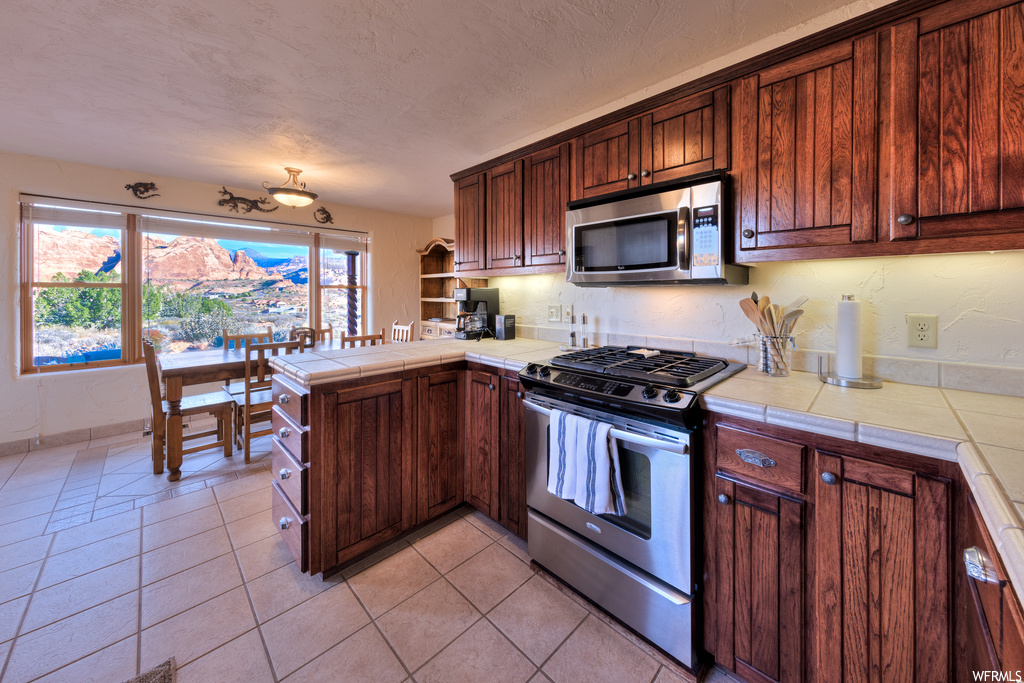 Kitchen with tile counters, stainless steel appliances, and light tile floors