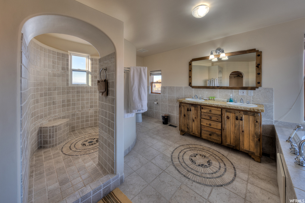 Bathroom featuring a healthy amount of sunlight, tile walls, plus walk in shower, and dual sinks