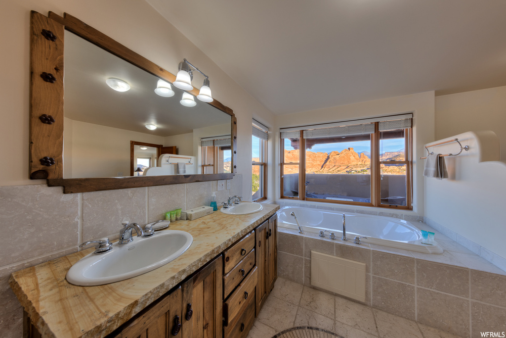 Bathroom featuring dual sinks, tasteful backsplash, tiled bath, oversized vanity, and tile floors