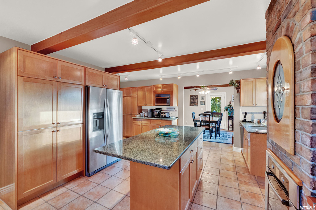 Kitchen with a center island, dark stone counters, stainless steel appliances, ceiling fan, and beamed ceiling