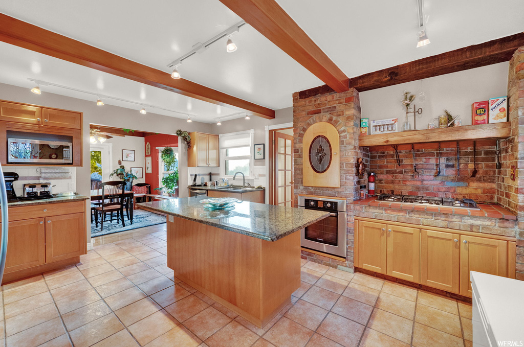 Kitchen with light tile flooring, beam ceiling, a kitchen island, and appliances with stainless steel finishes
