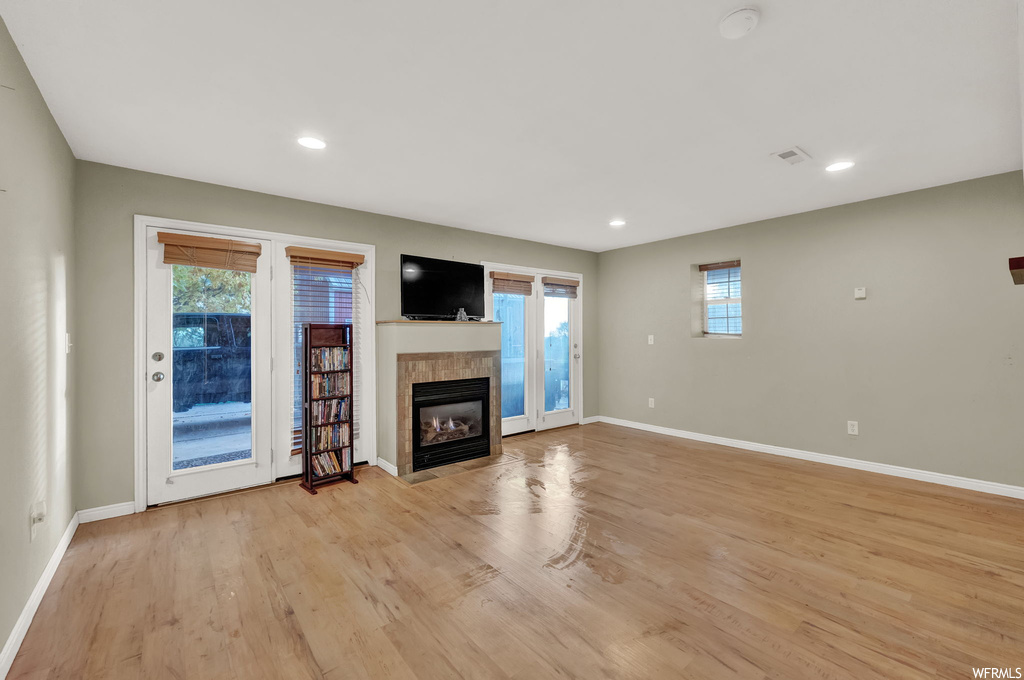 Unfurnished living room featuring a wealth of natural light, light hardwood / wood-style flooring, and a tiled fireplace