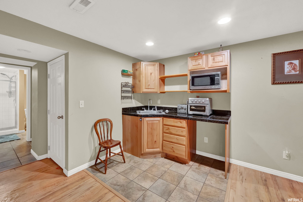 Kitchen with stainless steel microwave, light brown cabinetry, sink, and light tile floors